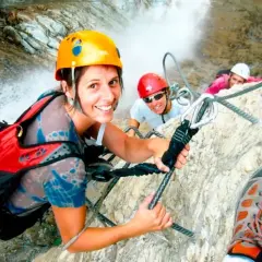 Kobieta w kasku i kamizelce asekuracyjnej na via ferracie, trzymająca linę.