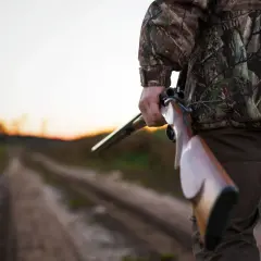 Myśliwy w kamuflażu trzyma strzelbę, gotów na polowanie indywidualne. Czy może zaprosić innych myśliwych?