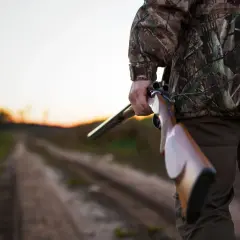Myśliwy w kamuflażu trzyma strzelbę na drodze. Czy myśliwy może polować na prywatnym terenie?