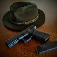 Na drewnianym stole leży ciemnozielony kapelusz myśliwski i pistolet z magazynkiem. Czy myśliwi mogą posiadać broń krótką?