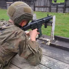 Osoba w mundurze i kasku celuje z karabinu na strzelnicy.