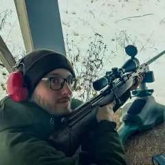 Mężczyzna w okularach i słuchawkach ochronnych celuje z karabinu. Czy myśliwi muszą brać udział w zawodach sportowych? Zima na strzelnicy.