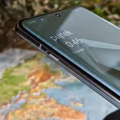 Zbliżenie na ekran telefonu z widocznym zegarem i mapą w tle.