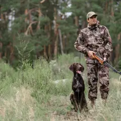 Myśliwy w kamuflażu z psem czeka na trop. Tak polują myśliwi, gotowi na każde wyzwanie w lesie.