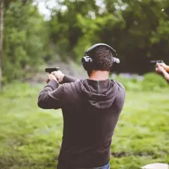 Dwóch mężczyzn w słuchawkach ochronnych strzela z pistoletów na strzelnicy plenerowej.