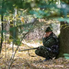 Myśliwy w lesie, zamyślony, z bronią. Czas na badania psychologiczne dla wszystkich myśliwych zbliża się nieubłaganie.