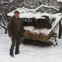 Mężczyzna w zimowym lesie przy paśniku z sianem.