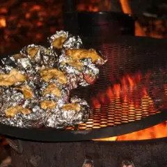 Ziemniaki zawinięte w folię aluminiową pieką się nad ogniskiem na metalowej kratce.