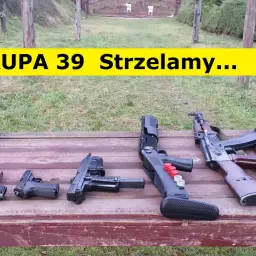 Na drewnianym stole leżą różne rodzaje broni palnej, w tle strzelnica.