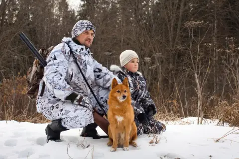 W gwarze myśliwskiej młody myśliwy z psem i dzieckiem w zimowym lesie, gotowi na polowanie.
