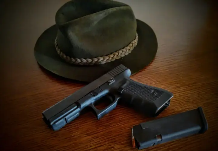 Na drewnianym stole leży ciemnozielony kapelusz myśliwski i pistolet z magazynkiem. Czy myśliwi mogą posiadać broń krótką?