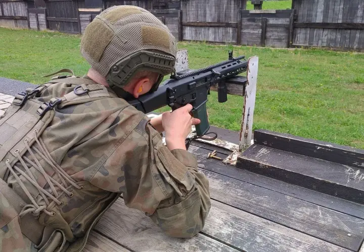 Osoba w mundurze i kasku celuje z karabinu na strzelnicy.