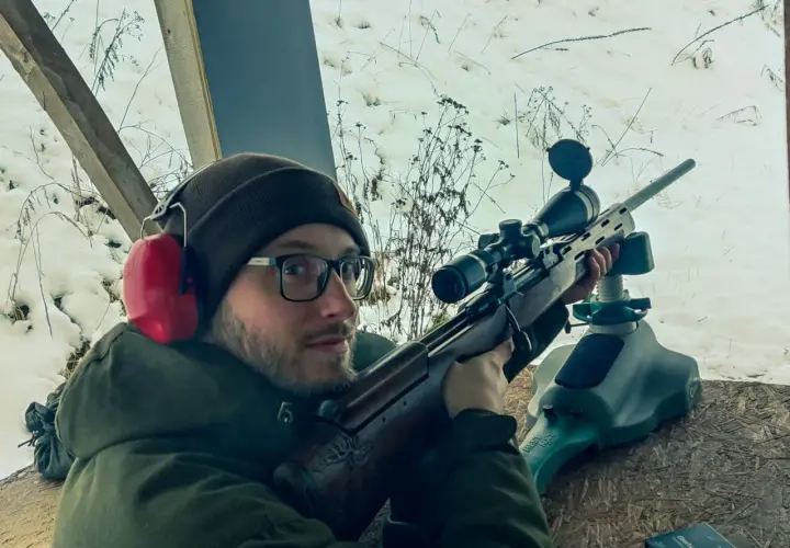 Mężczyzna w okularach i słuchawkach ochronnych celuje z karabinu. Czy myśliwi muszą brać udział w zawodach sportowych? Zima na strzelnicy.