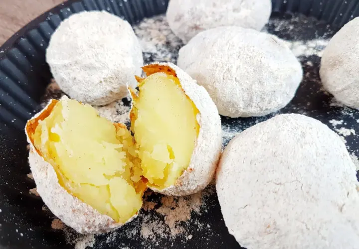 Ziemniaki pieczone w popiele, jeden przekrojony na pół, ukazujący miękki środek.