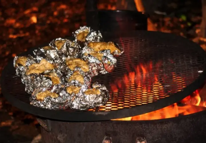 Ziemniaki zawinięte w folię aluminiową pieką się nad ogniskiem na metalowej kratce.