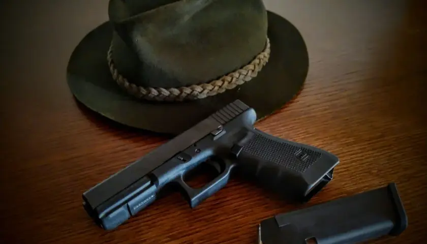 Na drewnianym stole leży ciemnozielony kapelusz myśliwski i pistolet z magazynkiem. Czy myśliwi mogą posiadać broń krótką?