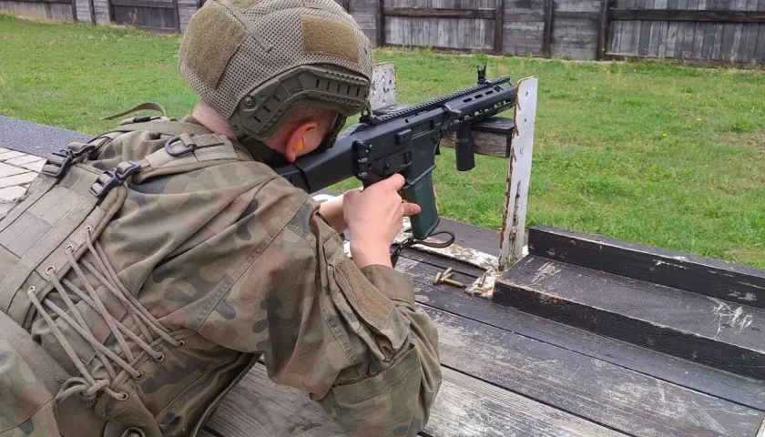 Osoba w mundurze i kasku celuje z karabinu na strzelnicy.