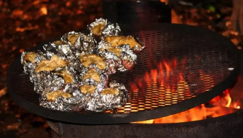 Ziemniaki zawinięte w folię aluminiową pieką się nad ogniskiem na metalowej kratce.