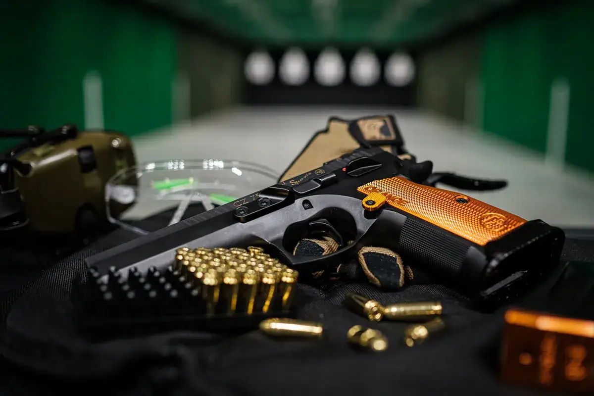 Pistolet CZ 75 SP-01 Shadow z pomarańczową okładziną, amunicją i ochronnikami słuchu na strzelnicy. Czy myśliwy może mieć broń krótką?
